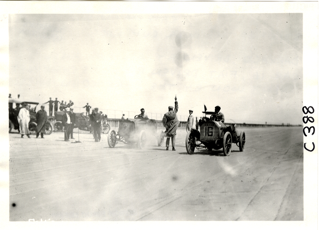 An old photo containing beach, people, cars