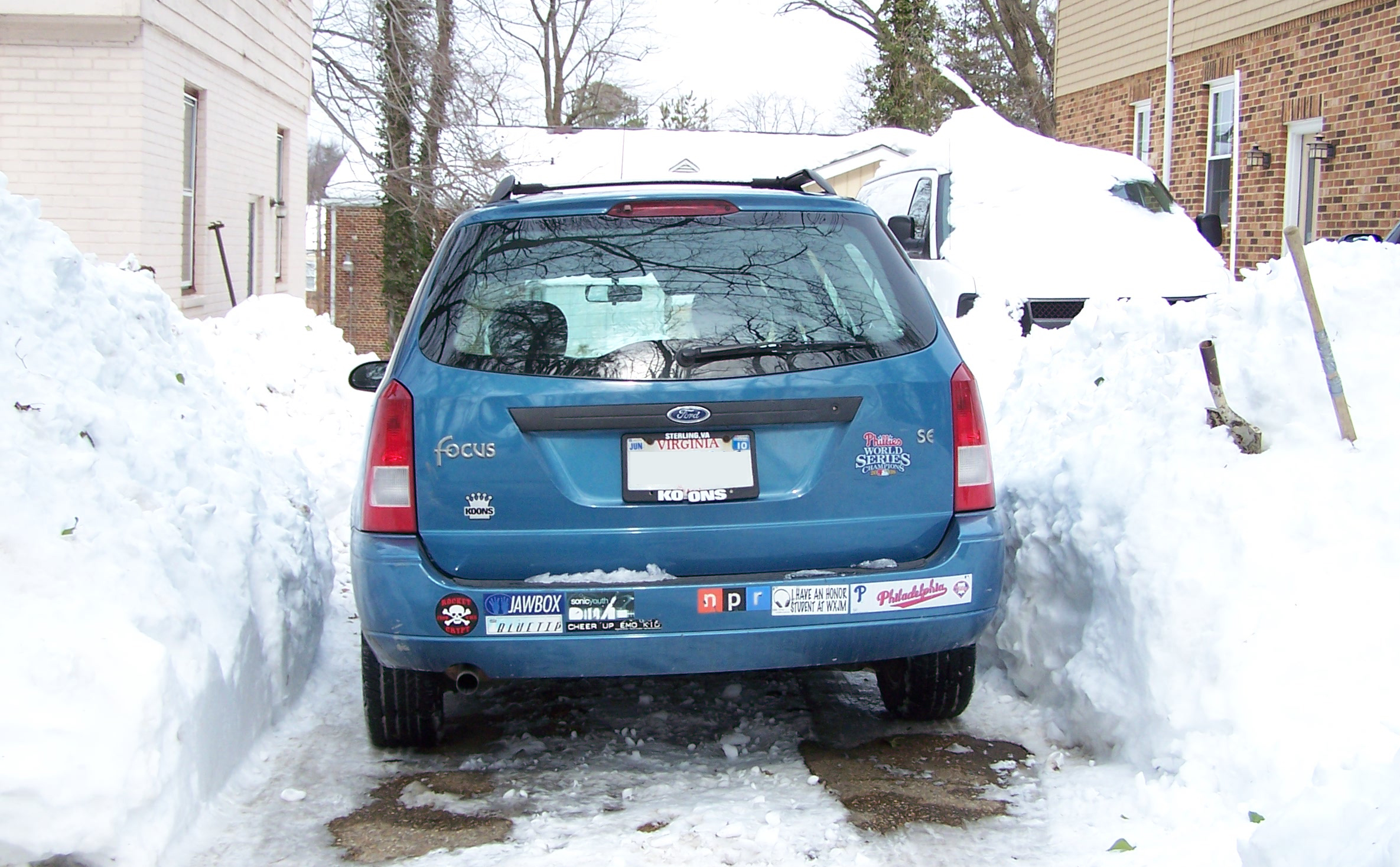 Photo of a car in a driveway cleared of snow, with snow piles around it
